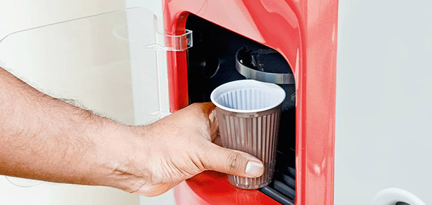 Hand greift an Kaffeebecher in Getränkeautomat
